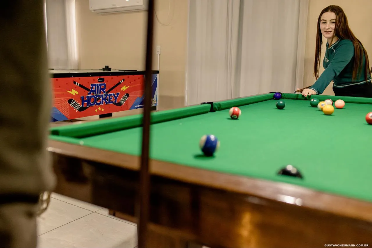 Mesa de sinuca montada com bolas coloridas e, ao fundo, a mesa de air hockey