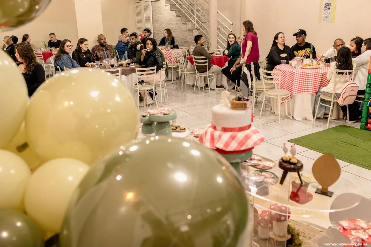 Convidados nas mesas de festa com toalhas xadrez, e o bolo com os doces em primeiro plano