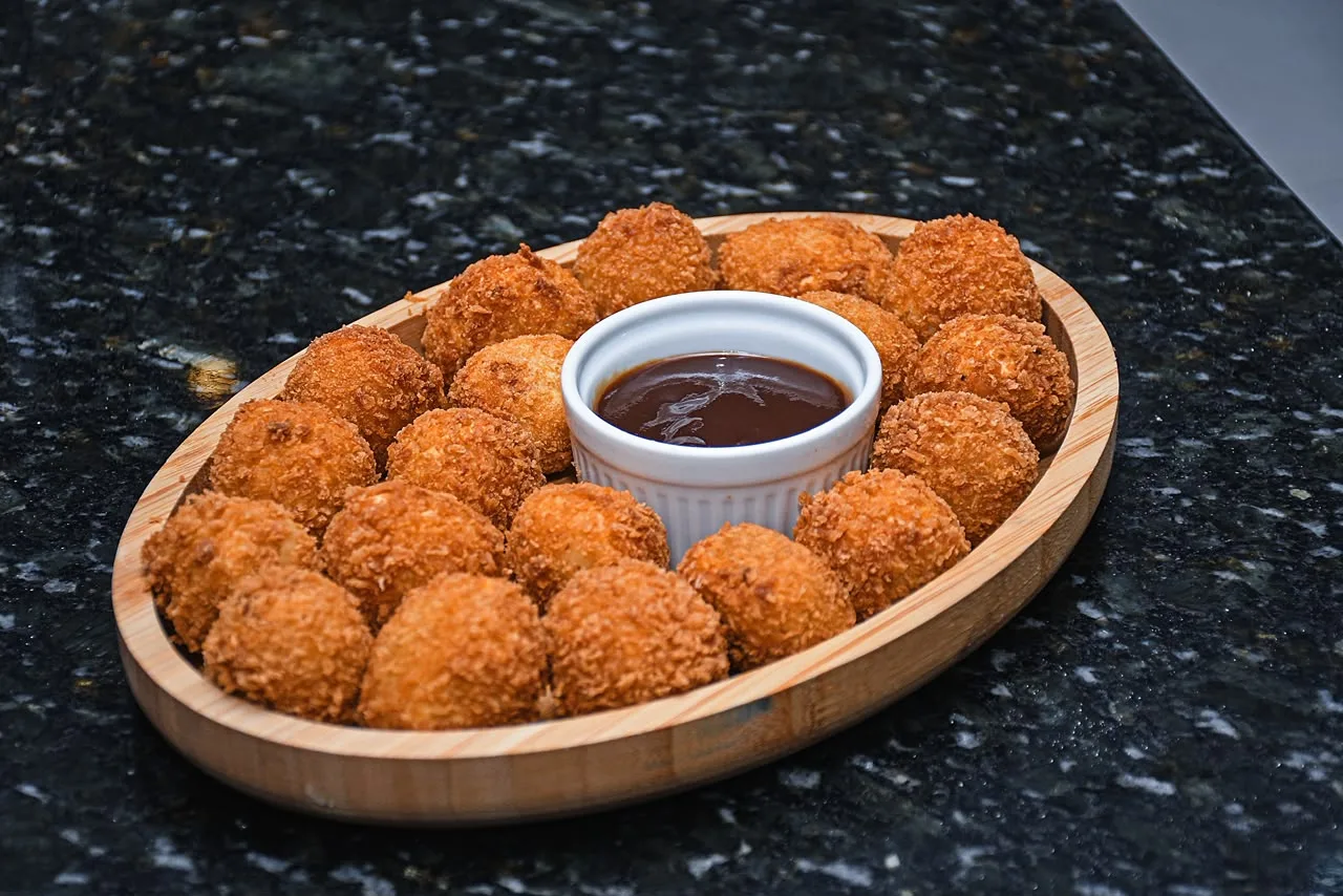 Coxinhas fritas servidas numa travessa de madeira oval, com molho no centro