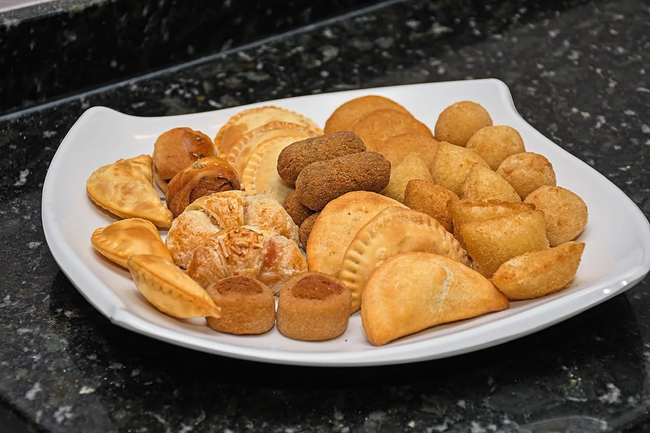 Prato branco com salgados variados: pastéis, bolinhas, risoles e croquetes