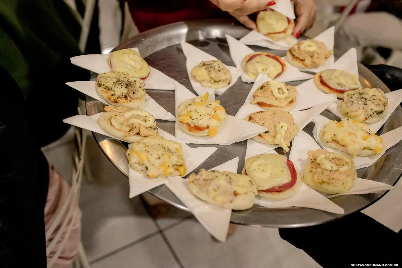 Bandeja redonda com mini pizzas variadas, segurada por uma mão com luva